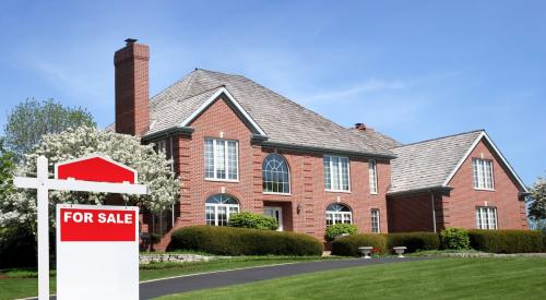 Red and white 'for sale' sign outside of large brick house