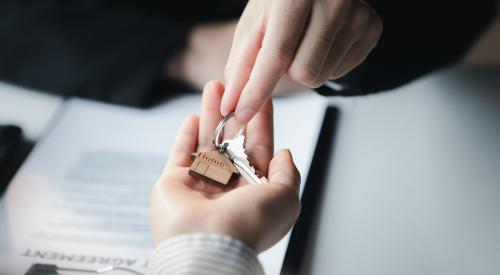 Builder handing silver house keys to buyer over work desk