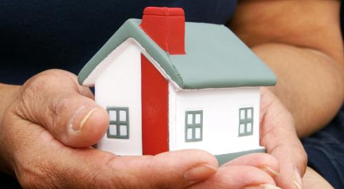Overlapping hands holding small white house model with red chimney