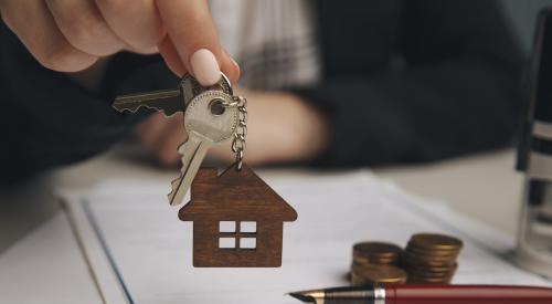 Person holding house keys above contract paperwork