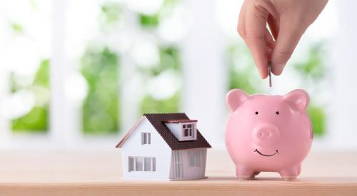 Person putting coin in piggy bank next to small house