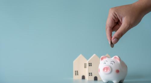 Person putting coin in piggy bank next to small wooden houses