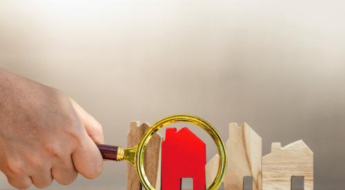 magnifying glass focused on one house painted red that stands out among other plain wood houses