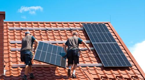 Workers installing solar panels on tile residential rooftop