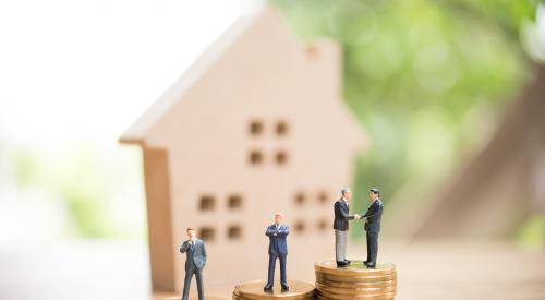 Small businessmen figurines on top of coin stacks with wooden home in background