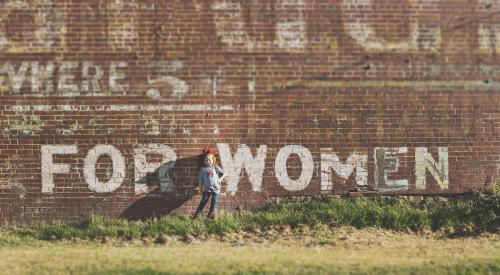 Little girl in front of brick wall that says "for women"