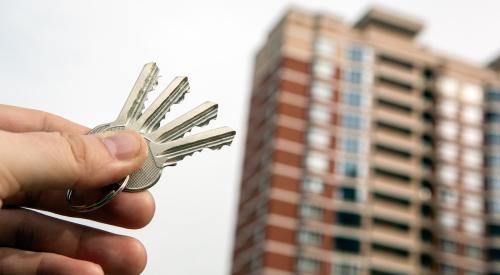 Person holding keys up to apartment building in background