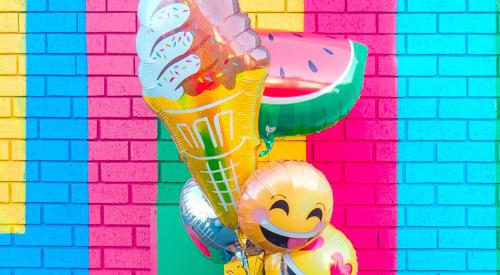 Person holding helium balloons in front of colorful brick wall