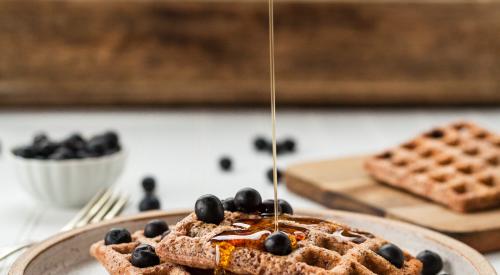 Pouring maple syrup on blueberry waffles
