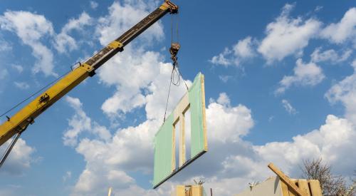 Wall of modular house on crane at job site