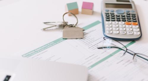 Mortgage application form surrounded by calculator, glasses, home keys, and laptop