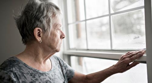 Elderly woman opening window in home and looking outside 