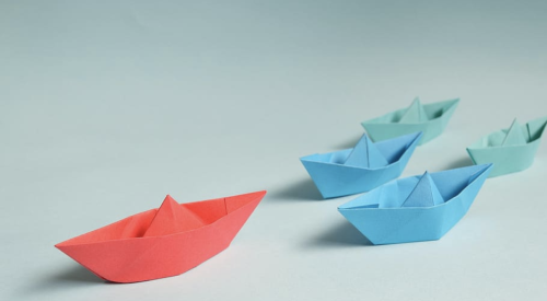 one red paper origami boat leading ahead of smaller blue origami boats 