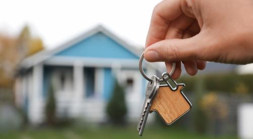 Person holding up house keys with blue house in background