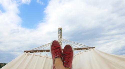 Man in hammock with red shoes looking up at clouds in blue sky