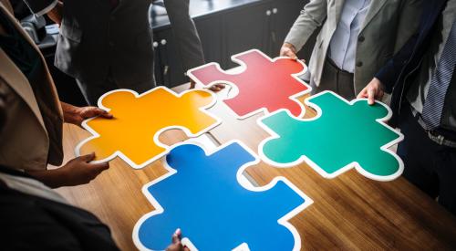 People in office holding up brightly colored, large puzzle pieces
