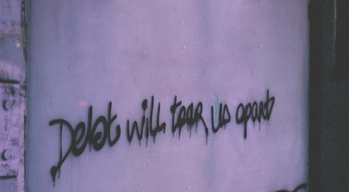 Graffiti on cement wall reads, 'debt will tear us apart'