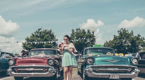 Woman with baby standing with vintage cars