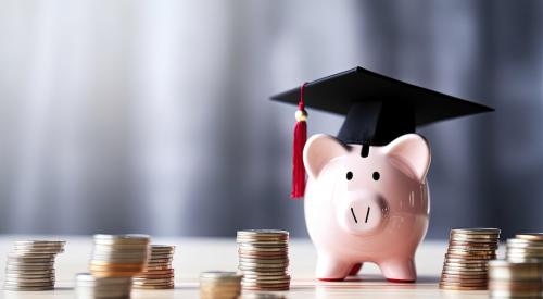 Piggy bank with graduation cap next to stacks of coins