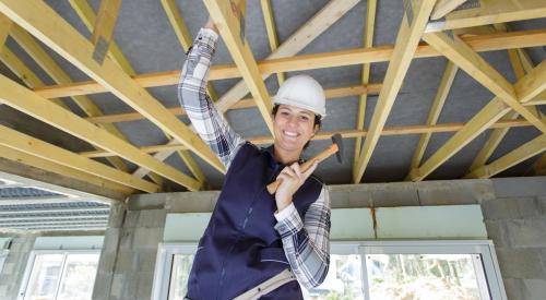 Woman standing beneath ceiling rafters in new house with hammer