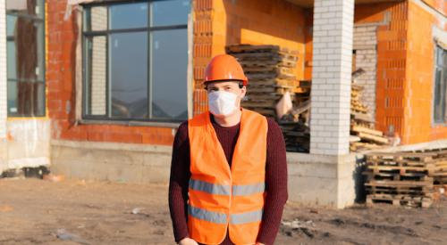 Worker at construction site wearing hard hat and protective face mask